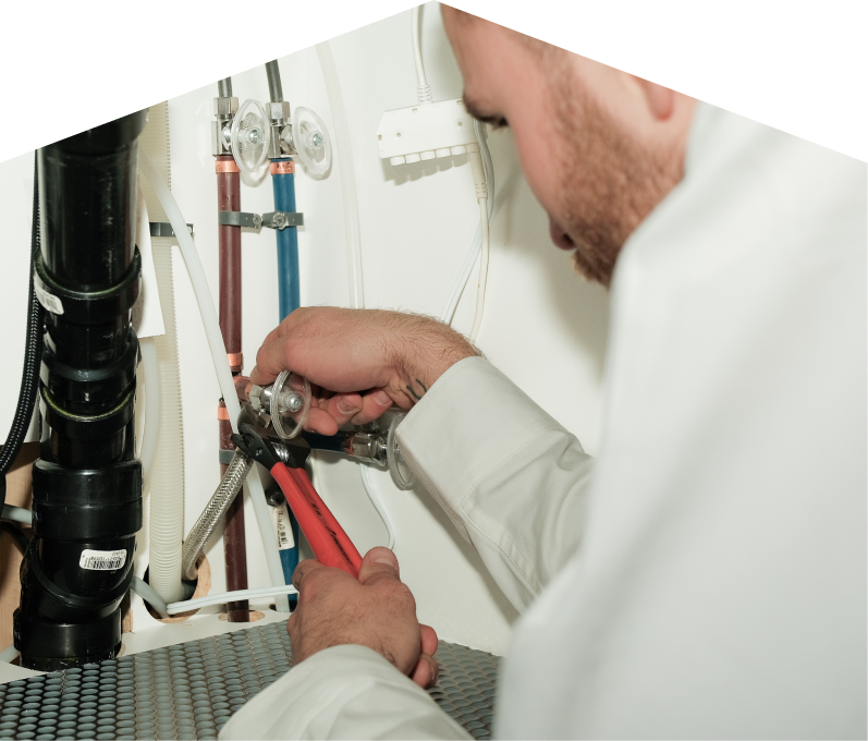 Haven Home plumbing expert tightening connections under a sink during a faucet installation, surrounded by hot and cold water supply lines and PVC drainage. Haven Home plumbing expert tightening connections under a sink during a faucet installation, surrounded by hot and cold water supply lines and PVC drainage.