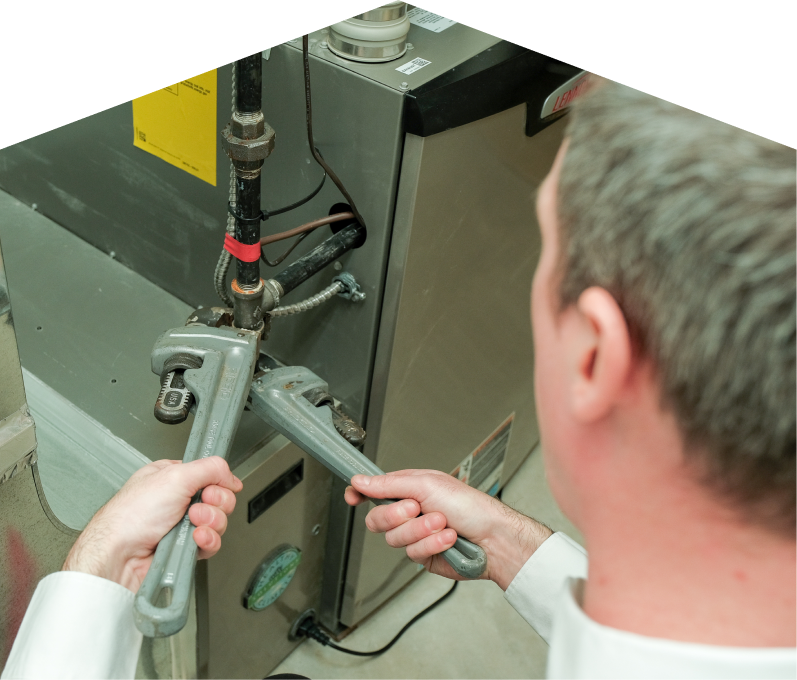 Haven Home plumbing specialist using two pipe wrenches to service a gas line connection beside a residential heating unit. Haven Home plumbing specialist using two pipe wrenches to service a gas line connection beside a residential heating unit.
