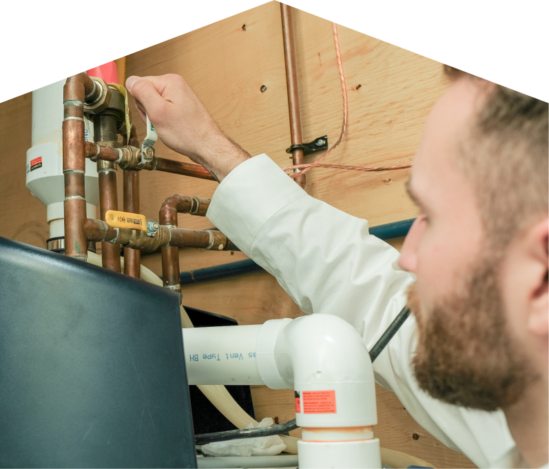 Haven Home water heater specialist tightens a valve on copper piping during a water heater installation, with exposed wood paneling and wiring in the background. Haven Home water heater specialist tightens a valve on copper piping during a water heater installation, with exposed wood paneling and wiring in the background.