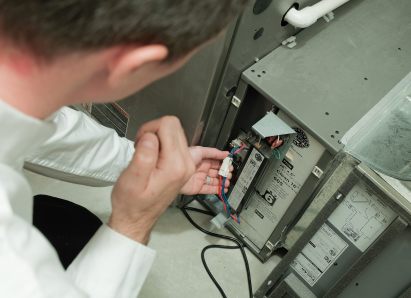 A Haven Home heating technician inspecting internal wiring during a service check on a residential heating unit. A Haven Home heating technician inspecting internal wiring during a service check on a residential heating unit.
