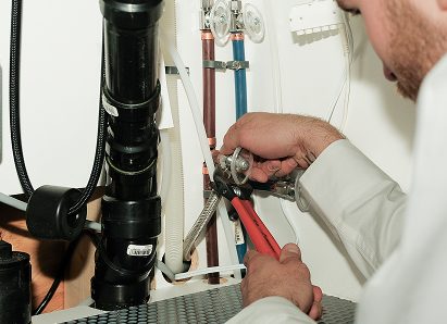 Using two pipe wrenches, a Haven Home professional plumber services a pipe connection near a vertical flue or vent pipe. Using two pipe wrenches, a Haven Home professional plumber services a pipe connection near a vertical flue or vent pipe.
