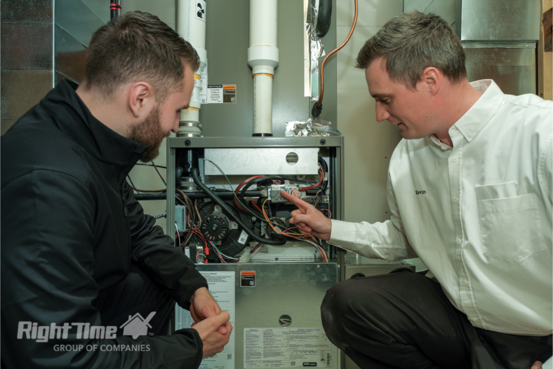 Two HVAC technicians in Kingston examining common HVAC problems in a heating and cooling system, discussing internal components and maintenance issues